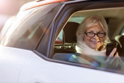 Senior woman with smartphone on the back seat of a taxi